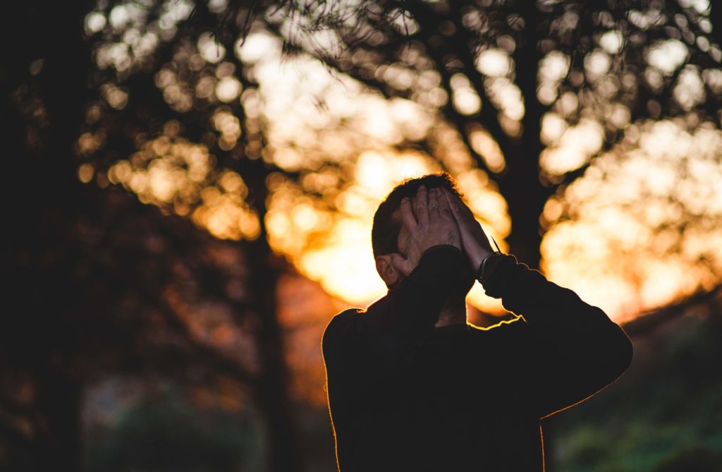silhouette pictured in forest at sunset with hands to face in stress