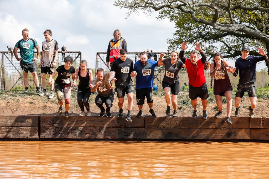 10 people lined up jump into a mud river for the Wolf Run